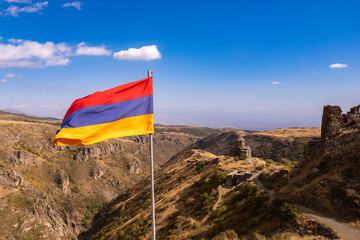 Aerial drone view to flag of Armenia and famous Vahramashen Church of the 11th century, near Amberd fortress in sunny summer day. Cliff with Arkashian River deep in canyon. Aragatsotn region, Armenia