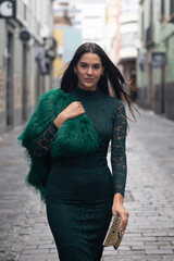 Fashionable woman walking down a city street, wearing a green lace dress and a gold clutch.