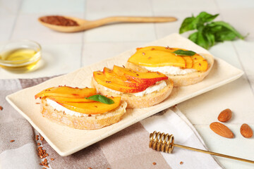 Plate of peach bruschetta with ricotta, flax seeds and mint on white tile background