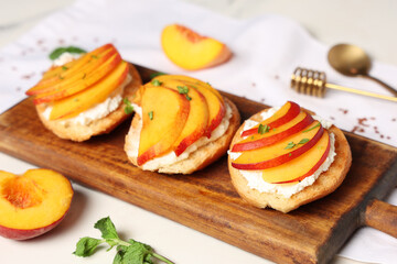 Wooden board of peach bruschetta with ricotta and mint on white background, closeup