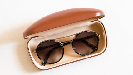 Beautiful modern sunglasses, made of brown with dark glasses, lie in an open box in the kit, isolated on a white background. 