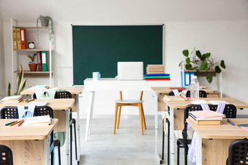 Interior of light classroom with blackboard, desks and backpacks