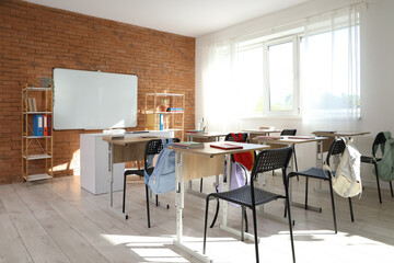 Interior of empty classroom with whiteboard, desks and shelf units