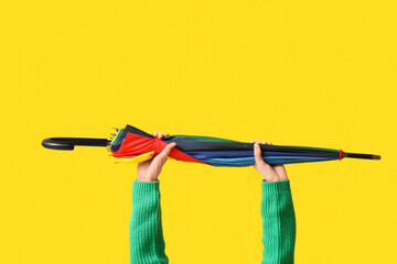 Female hands with stylish umbrella on yellow background