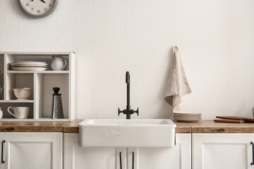 Sink on wooden counter and shelving unit near white wall in kitchen