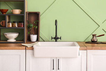 White ceramic sink and shelving unit on wooden counter near green wall in kitchen