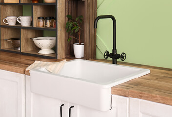White ceramic sink and shelving unit on wooden counter near green wall in kitchen