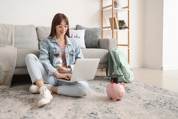 Female student with jar of money for college and laptop sitting at home. Education savings concept