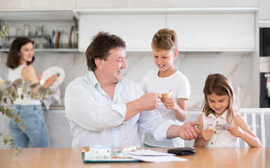 Adult man distributes money among family members sitting at table in kitchen