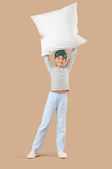 Cute little happy girl in pajamas with sleeping mask and pillow on beige background