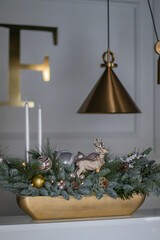 Christmas table composition made of fresh nobilis spruce, white candles, pine branches with glass balls and decorative gold deer. Happy New Year decorations.