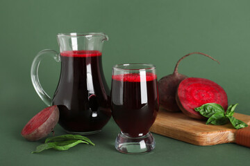 Glass and jug of fresh beet juice with basil on green background