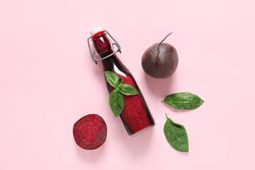 Bottle of fresh beet juice with basil and vegetables on pink background