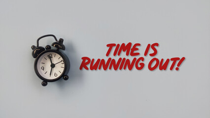 Conceptual black alarm clock with text TIME IS RUNNING OUT on grey background