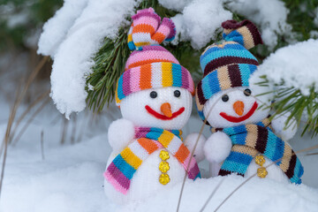 Snowman and snowwoman in christmas clothes stand under pine branch tree with white snow in winter forest. Knitted bauble. Christmas and new year holidays decoration. Symbol of festive winter season.