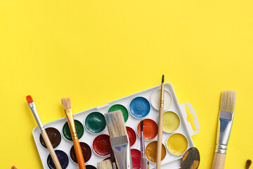 Artist brushes and paints on yellow background