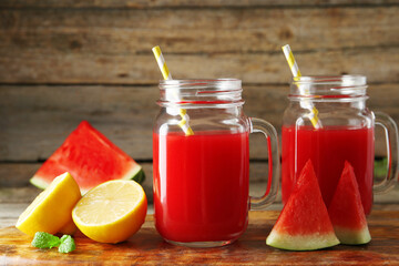 Tasty watermelon drink in mason jars and fresh fruits on wooden table, closeup