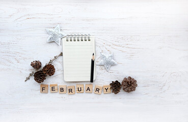 paper notepad, pencil, decorative stars, cones and word "february" of wooden letters on white wooden background. February month calendar concept. winter season. top view