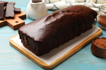 Tasty chocolate sponge cake and cocoa powder on light blue wooden table, closeup
