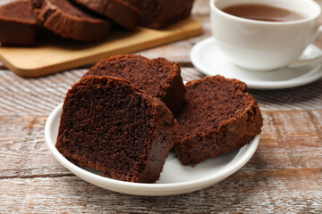 Slices of delicious chocolate sponge cake and tea on wooden table, closeup
