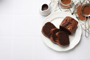 Delicious cut chocolate sponge cake and ingredients on white tiled table, flat lay. Space for text
