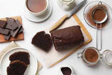 Delicious cut chocolate sponge cake and ingredients on white tiled table, flat lay