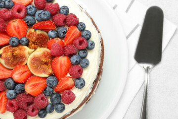 Delicious chocolate sponge cake with berries and server on light table, top view