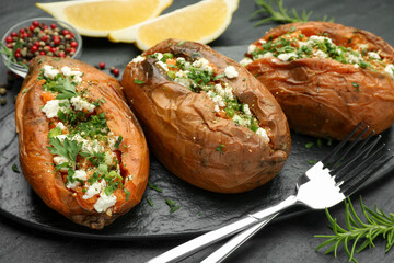 Tasty baked sweet potato with feta cheese and herbs on dark textured table, closeup