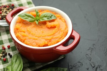 Tasty mashed sweet potato with basil in pot and spices on dark textured table, closeup