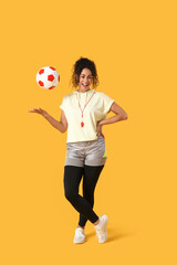 Naklejka premium Female African-American soccer trainer with ball on yellow background