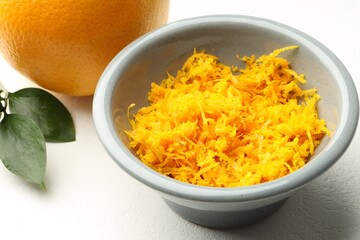 Fresh orange zest in bowl on light table, closeup