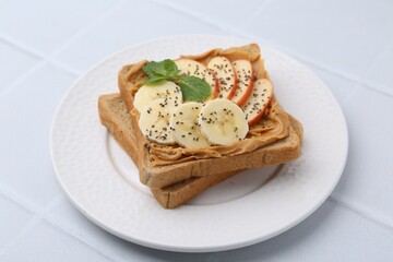 Tasty sandwich with peanut butter, apple, banana, chia seeds and mint on white table, closeup