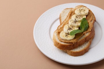 Tasty sandwich with peanut butter, banana, chia seeds and mint on brown background, closeup. Space for text