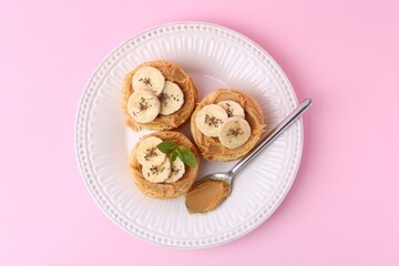 Tasty sandwiches with peanut butter, banana, chia seeds, mint and spoon on pink background, top view