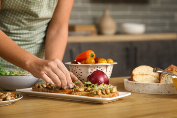 Young woman cooking vegan bruschettas at table in kitchen, closeup