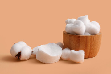 Wooden bowl with cotton balls, pads and flower on brown background
