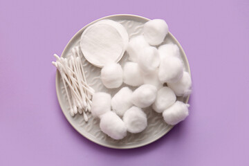 Plate with cotton balls, pads and swabs on lilac background