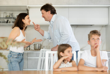 Angry parents quarrelling in the kitchen and bored preteen brother and little sister sitting at the...