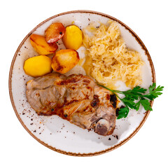 Grilled pork chop served with roasted potatoes and tangy sauerkraut garnished with parsley. Isolated over white background