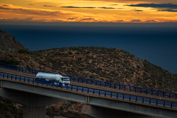 Fuel tanker truck driving at dawn on a bridge, with the sea in the background on the horizon.