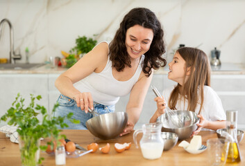 Happy mother and her daughter whisking ingredients in a bowl using metal corolla in the kitchen