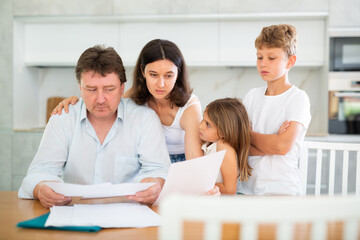 Obraz premium Upset adult man looking at documents while sitting in kitchen with his family