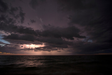 Sunset landscape of rainstorm with lightning and thunder over sea water waves crushing on sandy beach. Beautiful seascape in evening