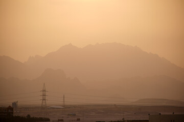 Sunset landscape with dark mountain peaks in egyptian desert and high voltage power lines
