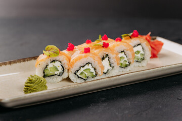 Close-up of sushi rolls with salmon, cream cheese, and cucumber, garnished with wasabi and roe