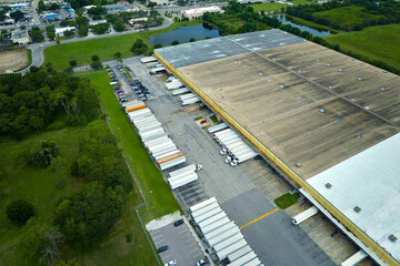 Top view of giant logistics center with many commercial trailer trucks unloading and uploading retail products for further shipment. Global economy concept