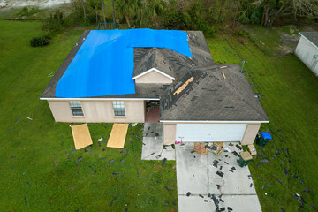 Top view of leaking house roof covered with protective tarp sheets against rain water leaks until...