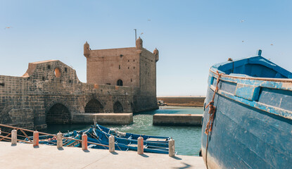 Historical port of Essaouira, Morocco with blue fishing boats docked beside famous ancient fortress...