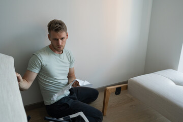a man reads instructions on how to assemble a sofa at home by himself