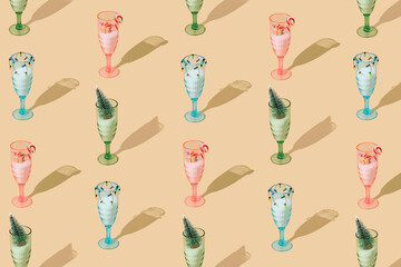 Christmas pattern made of colorful wine and cocktail glasses with snow and Xmas decorations on pastel cream background. Minimal Christmas and New Year party concept. Creative festive holiday backdrop.
